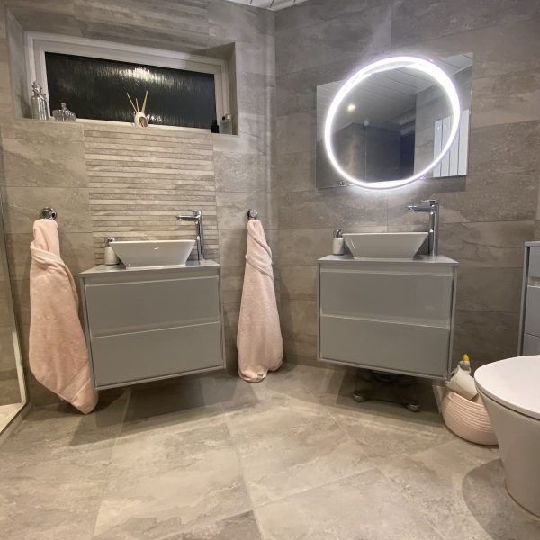 Grey sinks in bathroom with circular backlit mirror